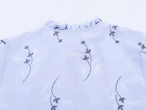 Detail van de ruffelkraag en het borduurwerk van bladeren op een lichtblauwe blouse