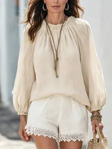 Model trägt eine beige Bluse mit Laternärmeln und weiße Spitzenshorts im Freien.