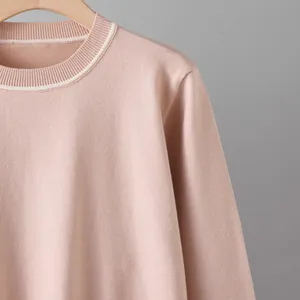 Detail of pink knit sweater featuring a white striped contrast round neckline on hanger