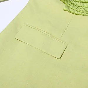 Close-up of light green blazer featuring a detailed pleated ruffle and flap pocket.