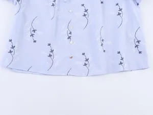 Detail van een lichtblauw shirt met bloemenborduurwerk en witte knopen