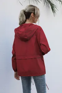 Back view of a lightweight dark red hooded rain jacket for women in outdoor setting