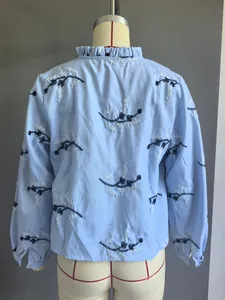 Achterkant detail met fijn zwart en wit borduurwerk op een lichtblauwe blouse met ruches