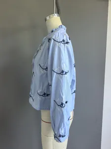Zijaanzicht van een lichtblauwe blouse met lange mouwen en borduursel op een mannequin