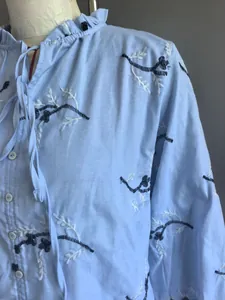 Detailopname van een lichtblauwe damesblouse met bloemenborduursel en ruches kraag