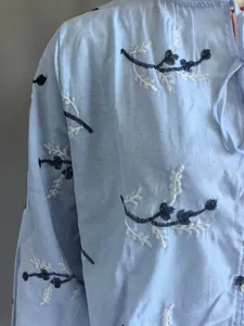 Detailopname van wit en marineblauw bloemenborduurwerk op een lichtblauwe katoenen blouse