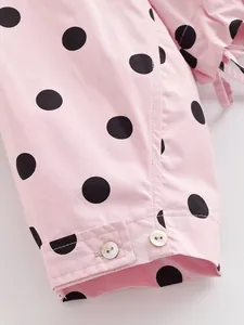Close-up detail of a pink jacket sleeve featuring black polka dots and white buttons