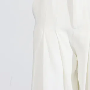 Close-up detail showing the refined pleated tailoring on white wide-leg trousers for women