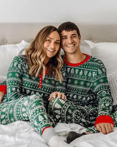 Couple heureux portant un pyjama de Noël assorti vert et rouge avec motifs sapins sur un lit
