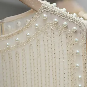 Close-up detail of champagne sleeveless vest with heavy pearl and bead embroidery