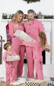 Familia feliz con pijamas navideños de rayas rojas y blancas abriendo regalos junto al fuego