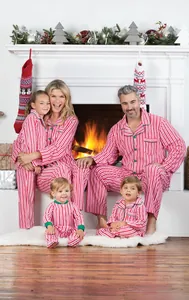 Conjunto de pijamas navideños a rayas rojas y blancas para familia frente a una chimenea