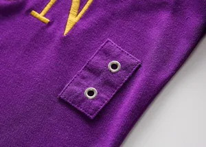 Macro detail of purple cotton polo shirt showing metal eyelets and yellow embroidery