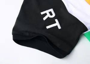 Détail de la broderie des lettres RT sur la manche d'un polo noir en coton piqué
