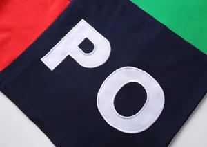 Gros plan sur les lettres PO brodées en blanc d'un polo en coton à blocs de couleur