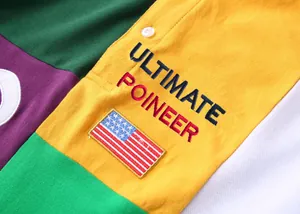Détail de la broderie Ultimate Poineer et du drapeau US sur polo en blocs de couleurs