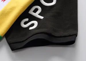 Dettaglio ricamo bianco su manica di polo in cotone color-block nero e giallo