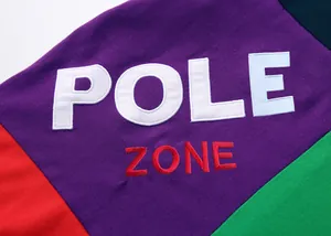 Vue rapprochée d'un polo patchwork multicolore avec broderie POLE ZONE détaillée.
