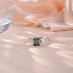 Détail d'une bague en moissanite bleu-vert de 6x8mm sur un tissu en soie délicate.