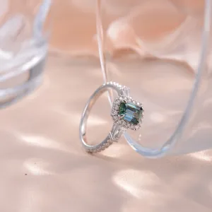 Close-up detail showing the emerald-cut green moissanite stone and silver halo setting