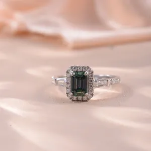 Detailed macro view of emerald-cut green moissanite halo ring with side trapezoid diamonds