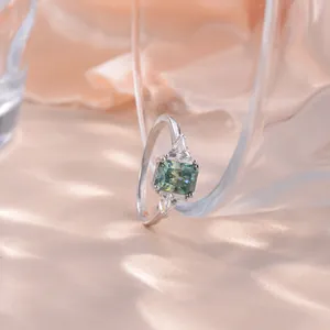Détail d'une bague avec moissanite bleu-vert taille radiant et pierres triangulaires.