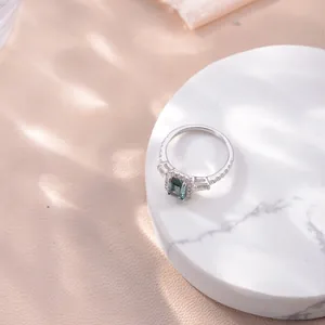 Detailed view of an emerald-cut green moissanite halo ring on a white marble stand