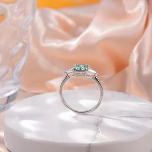 Bague élégante en moissanite bleu-vert taille radiant exposée sur un socle en marbre.