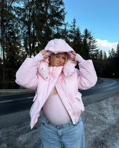 Modieuze roze winterjas met capuchon voor dames in een besneeuwde bosrijke buitenomgeving