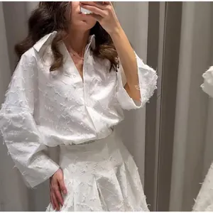 Dettaglio della trama a frange su un set elegante di camicia e gonna bianchi