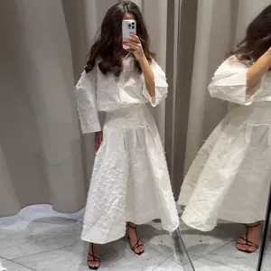 Dettaglio di un completo a due pezzi con camicia bianca a frange e gonna midi a trapezio