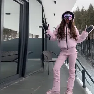 Stylish women's pink hooded ski suit including jacket and pants in snowy resort
