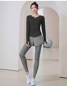 Vollansicht einer Frau in einem schwarzen langärmeligen Sportoberteil und grauen Yoga-Leggings