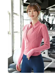 Donna con maglia sportiva rosa a maniche lunghe e leggings blu in una palestra di fitness.