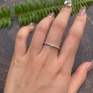 Close-up view of a delicate silver cross ring with pavé moissanite stones on a finger