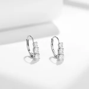 Close-up of elegant silver three-stone moissanite lever-back earrings on white surface