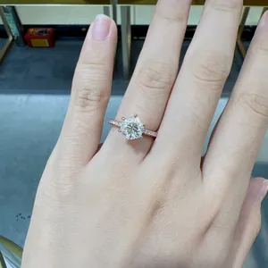Close-up view of a sparkling round moissanite engagement ring on a finger in rose gold finish.