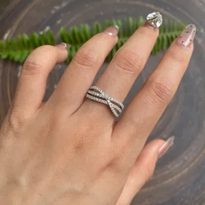 Close-up van een zilveren gekruiste moissaniet ring met opengewerkt design om de vinger.