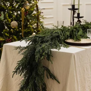Realistische kerstslinger van dennennaalden gedrapeerd over een feestelijke tafel.