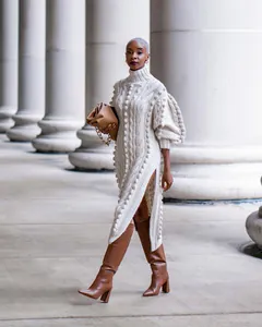 Detailed view of high-neck cable knit dress with side slit and pom-pom texture.