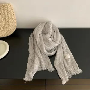 Detail view of light grey pleated cotton-linen scarf with fringed edges and label