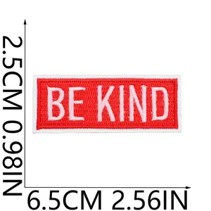 Détail de l'écusson brodé rouge BE KIND avec dimensions 6,5x2,5cm 2,56x0,98in.