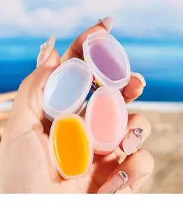 Close-up detail of four colorful moisturizing lip masks held in a hand at the beach.