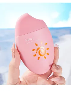 Gros plan d'un flacon de crème solaire rose tenu par une main devant une plage ensoleillée
