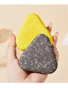 Close-up of hand holding yellow and charcoal triangular scented bath soaps for deep cleaning