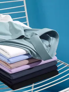 Stapel kleurrijke herenpolo's met korte mouwen op een wit rek tegen een blauwe wand.