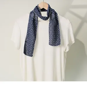 Detail view of a navy blue cotton-linen skinny scarf with white clover print on a white shirt.
