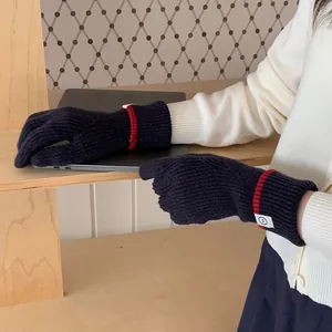 Detailed view of navy blue knitted gloves with red trim and smiley patch on wrist.