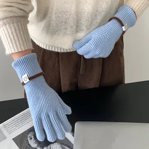 Detailed view of light blue knitted winter gloves featuring brown trim and white patch label