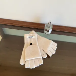 Detail of cream flip-top knitted wool gloves with label on a wooden table setup